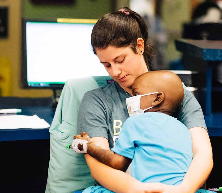 pediatric cancer patient boy sits on nurses lap after chemotherapy